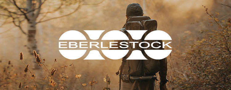 Person mit grossem Trekkingrucksack auf schmalem Waldweg imHerbst, Eberlestock Logo mittig eingeblendet.