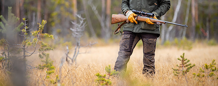 Jäger mit Jagdhosen und Gewehr auf Wiese vor Wald