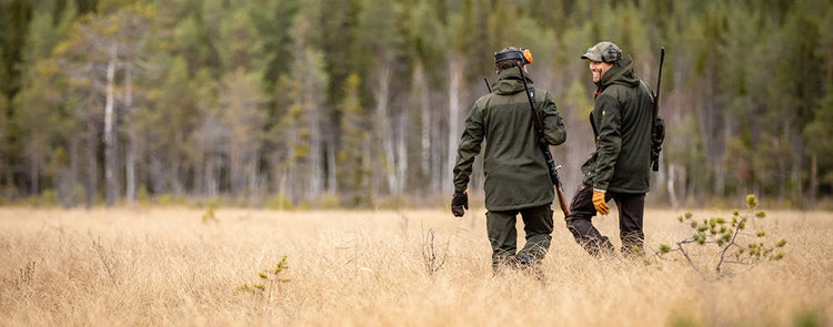 Zwei Jäger mit Jagd Jacken unterhalten sich auf Wiese vor Wald